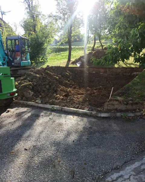Bager izkopava brežino ob robu gozda