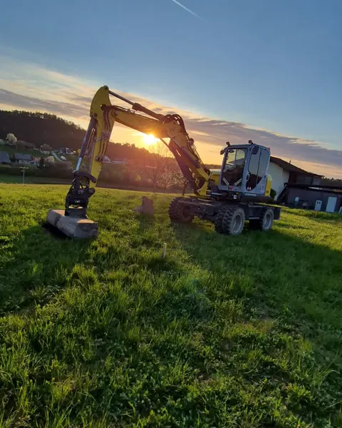 Kolesni bager Wacker Neuson na travniku ob sončnem zahodu