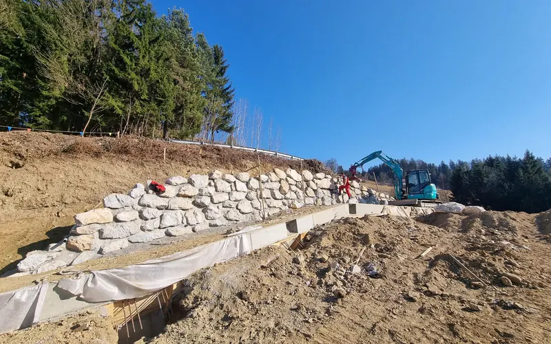 Gradnja kamnite škarpe z bagrom, za zidom geotekstil in drenaža